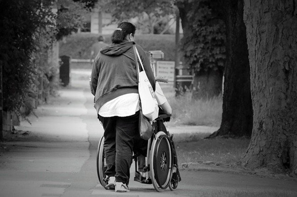 photo d'une personne qui pousse dans un fauteuil roulant une personne à mobilité réduite
